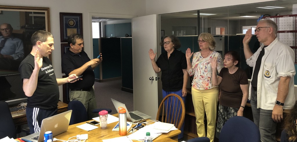 Andy Schotz, left, asks the remaining new board member to raise their right hands and repeat the oath after him. This was at the July 6, 2019, board retreat held at Warren Communications News, the workplace of Immediate Past President Jonathan Make. From the left, the new officers are Recording Secretary Kathryn Foxhall, and at large board members Denise Dunbar, Celia Wexler and Dan Kubiske. President Randy Showstack prepares to snap a photo of the proceeding.